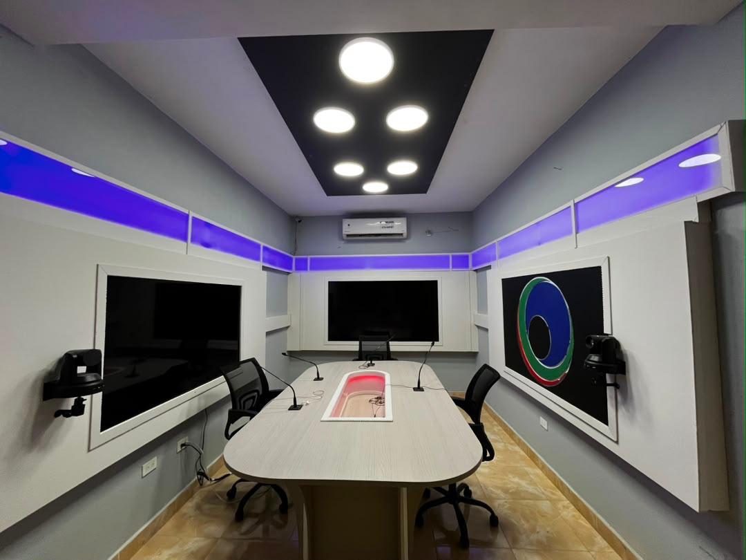Studio de Radio Télé Cool avec sa table de discussion, ses microphones et le logo de la station.